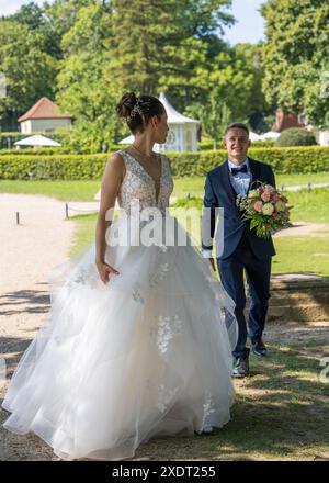Wunderschöne Braut und Bräutigam auf einem Spaziergang. Die junge Braut steht halb gedreht und schaut zärtlich den Bräutigam an, der den Hochzeitsstrauß in den Händen hält. Newl Stockfoto