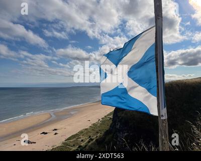 Nationale blau-weiße schottische Flagge, die im Wind auf einem Mast fliegt und auf dem Meer in der Ferne flattert Stockfoto