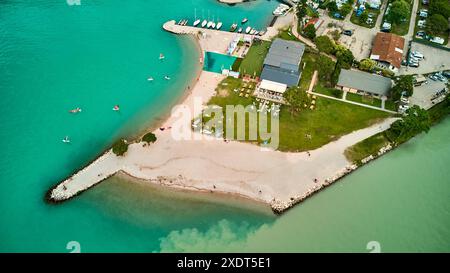 Torbole, Gardasee, Italien - 24. Juni 2024: Badestrand am Gardasee in der Gemeinde Torbole, nahe Riva. Aus der Vogelperspektive auf die Surfer am Strand, wo der Fluss Sarca in den See am Gardasee fließt, mit wirbelndem, fließendem, verschmutztem Wasser. *** Badestrand am Gardasee bei der Gemeinde Torbole, nahe Riva. Luftaufnahme von Surfern am Strand bei der Einmündung des Flusses Sarca in den See am Lago di Garda mit aufgewirbeltem, strömendem verschmutzen Wasser. Stockfoto