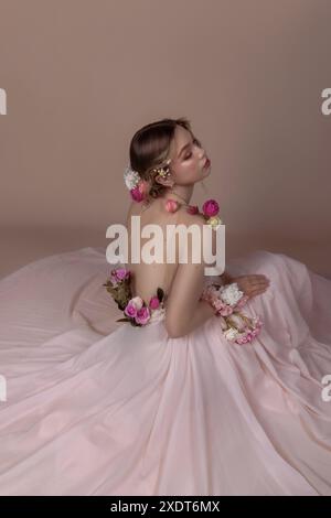 Eine Frau in einem rosafarbenen Kleid mit Blumen sitzt auf dem Boden in einem Studio. Stockfoto