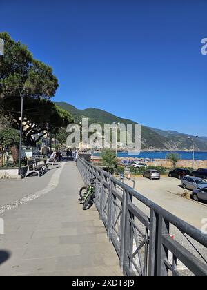 Ruhiger Blick auf die Straße von der Strandpromenade mit Parkplatz in Monterosso, Italien. Ältere, nicht erkennbare Menschen, die auf Bänken ruhen. Frau, die am Telefon spricht Stockfoto