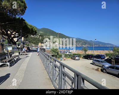 Ruhiger Blick auf die Straße von der Strandpromenade mit Parkplatz in Monterosso, Italien. Ältere, nicht erkennbare Menschen, die auf Bänken ruhen. Frau, die am Telefon spricht Stockfoto