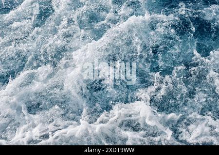 Meereswellen, Blasen und weißer Schaum über dem blauen Meer, geformt durch den Motor eines Motorbootes. Stockfoto