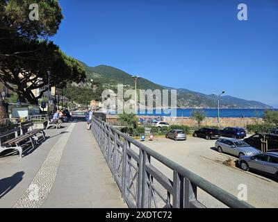 Ruhiger Blick auf die Straße von der Strandpromenade mit Parkplatz in Monterosso, Italien. Ältere, nicht erkennbare Menschen, die auf Bänken ruhen. Frau, die am Telefon spricht Stockfoto