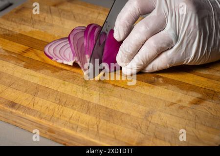 Ein Koch schneidet rote Zwiebeln auf hölzernem Schneidebrett. Studio-Aufnahme Stockfoto