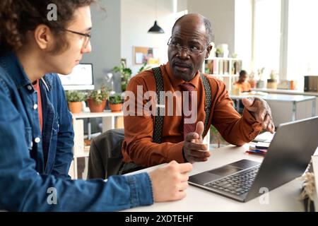 Porträt eines hochrangigen afroamerikanischen Mannes, der mit jungen Kollegen an einem altersumfassenden Arbeitsplatz spricht und das Konzept des Spätpensionierungsprojekts diskutiert Stockfoto