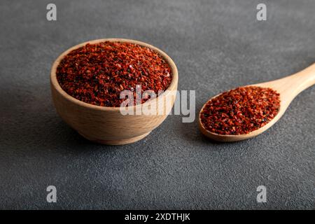 Rote Pfefferflocken. Rote Chilischoten in Holzschale auf grauem Hintergrund Stockfoto