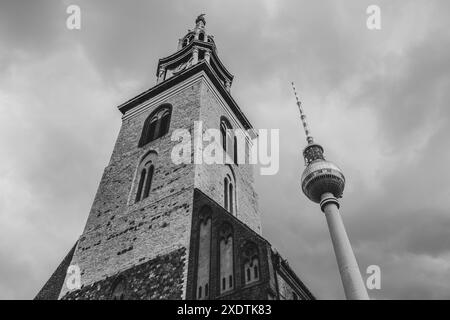 Die Marienkirche steht mit dem berühmten Berliner Fernsehturm vor einem dramatischen Himmel. Berlin, Deutschland. Schwarzweißbild... Schwarzweißbild. Stockfoto