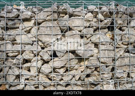 Gabion, ein Zaun aus Meeressteinen und großem blauem Glas in einer Maschenöffnung. Landschaftsgestaltung, Bauzäune, dekoratives Design für Baustellenräumung. Hohe qu Stockfoto