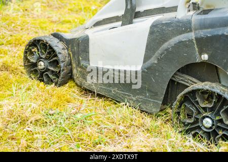 Ein grauer Rasenmäher auf dem grünen Gras im Park. Nahaufnahme. Mähen von Gras mit einem elektrischen Mäher. Schneiden Sie den Rasen. Reinigung des Gartens. Hochwertiges Foto Stockfoto