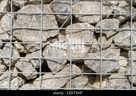 Gabion, ein Zaun aus Meeressteinen und großem blauem Glas in einer Maschenöffnung. Landschaftsgestaltung, Bauzäune, dekoratives Design für Baustellenräumung. Hohe qu Stockfoto