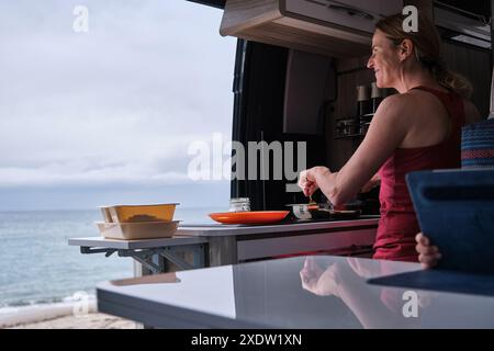 Eine Frau, die in ihrem Wohnmobil mit Meerblick kocht Stockfoto