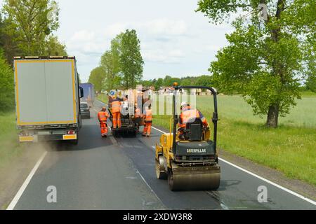 Tarnow, Polen - 19. Mai 2023: Ein Team von Arbeitern in gut sichtbarer Kleidung setzt schwere Maschinen ein, um neuen Asphalt auf einer Landstraße zu legen Stockfoto