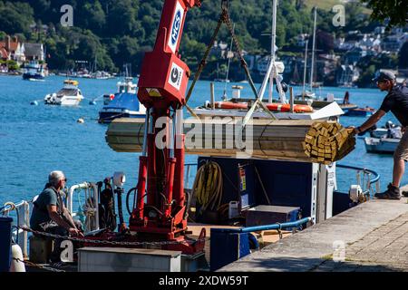 Arbeiter, die Holz auf ein Boot mit einem Kran an einem Dock mit malerischem Flussgrund laden. Dartmouth Devon UK Stockfoto