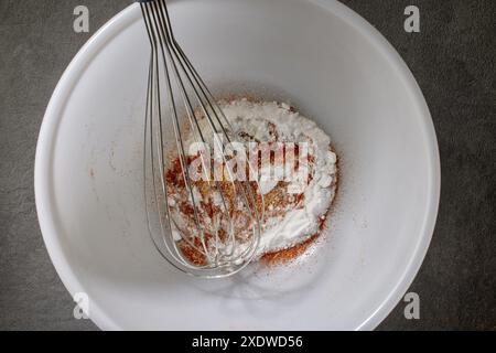 Gewürze mit Salz und Backpulver werden in einer weißen Schüssel auf dem Küchentisch, Blick von oben, gemischt. Verfahren zur Herstellung knuspriger Hühnerflügel Stockfoto