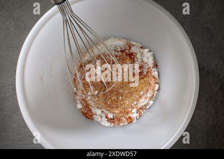 Gewürze mit Salz und Backpulver werden in einer weißen Schüssel auf dem Küchentisch, Blick von oben, gemischt. Verfahren zur Herstellung knuspriger Hühnerflügel Stockfoto