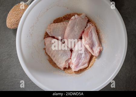 Frische, rohe Hähnchenflügel in einer Schüssel verschiedener Gewürzmischung. Verfahren zur Herstellung knuspriger Hähnchenflügel Stockfoto