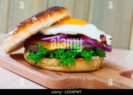 Burger mit Spiegelei, Speck, Käse, Zwiebeln und Salat Stockfoto