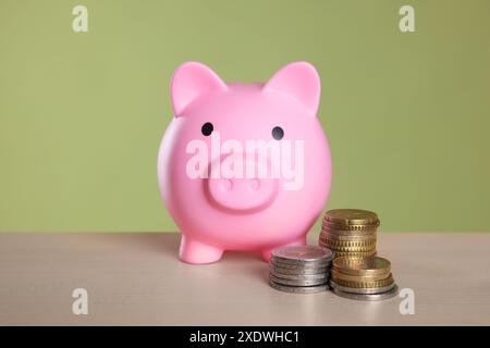 Rosafarbene Schweinebank und Münzen auf Holztisch vor olivem Hintergrund Stockfoto