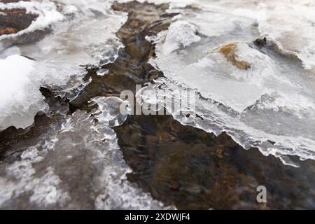 Ein schmaler kleiner Fluss im Winter, bedeckt mit Schnee und Eis, das Eis auf dem Fluss ist mit einem Kunststoff-geogitter verstärkt Stockfoto