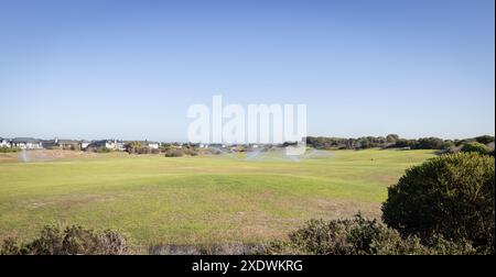Sprinkler bewässern grünen Rasen in Vorstadtviertel an sonnigen Tagen, Kopierraum Stockfoto