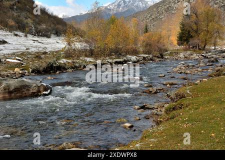 Ein kleiner stürmischer Fluss fließt von den Bergen entlang des gelblichen Waldes, der an einem sonnigen Herbstmorgen mit dem ersten Schnee bestreut ist. Yaloman River, A Stockfoto