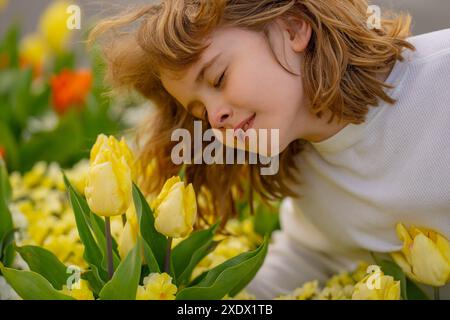 Süßes, hübsches blondes Kind mit geschlossenen Augen, stinkende Tulpenblüte im Spring Park. Das Kind riecht Tulpen im Frühlingsgarten. Süßer kleiner Junge, der Tulpe hält Stockfoto