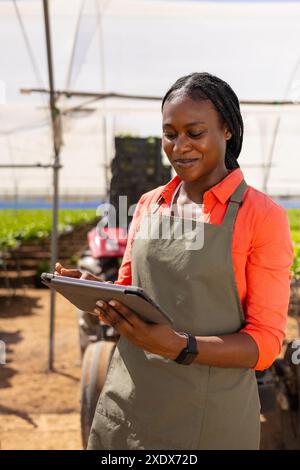 Afroamerikanische Farmerin, die Tablette für die Verwaltung von hydroponischen landwirtschaftlichen Betrieben verwendet Stockfoto