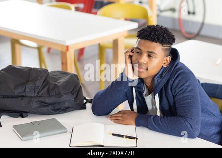 In der Schule träumte ein männlicher afroamerikanischer Schüler am Schreibtisch mit Notizbuch und Stift, Kopierraum Stockfoto