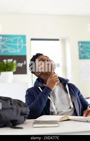 In der Schule denkt ein afroamerikanischer Schüler, während er den Stift im Klassenzimmer hält Stockfoto