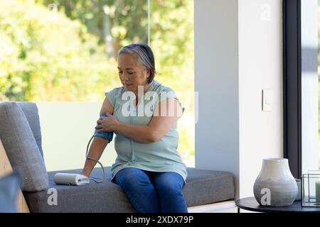 Ältere Frau, die zu Hause mit digitalem Monitor den Blutdruck misst Stockfoto