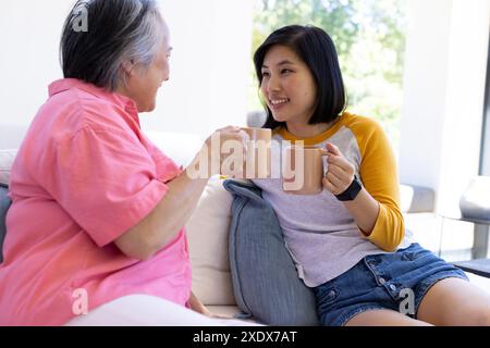 Mutter und Tochter genießen Kaffee, sitzen auf der Couch, lächeln und reden Stockfoto