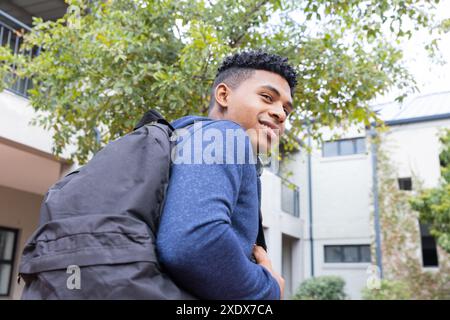 Mit Rucksack und Lächeln, männlicher afroamerikanischer Schüler blickt draußen in die Schule Stockfoto