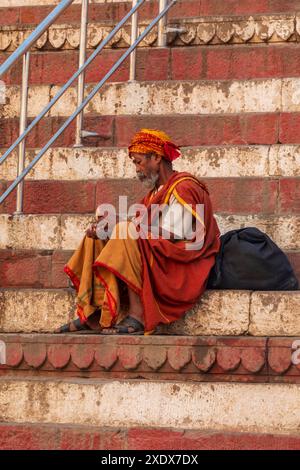 Indien, Uttar Pradesh, Varanasi, Bangali Tola. Mukesh Ghat. Mann, der auf einer Treppe sitzt. Stockfoto