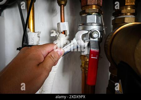 Der Klempner zieht mit einem verstellbaren Schraubenschlüssel eine Mutter an einer Leitung des Warmwasserbereiters fest. Stockfoto