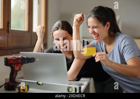 Zwei aufgeregte Mitbewohner feiern den Online-Kauf mit Kreditkarte und Laptop Stockfoto