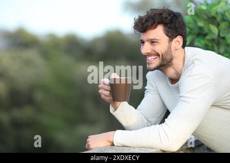 Glücklicher Mann auf einer Terrasse, der Kaffee trinkt und sich daheim verlässt Stockfoto