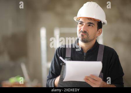 Enttäuschter Bauarbeiter, der die Arbeit überprüft und sich Notizen macht, wenn er oben hinsieht Stockfoto