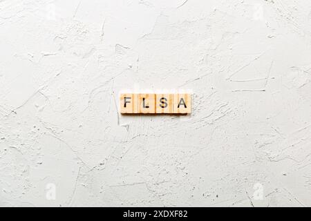 FLSA-Wort auf Holzblock geschrieben. Text des Fair Labor Standards Act auf dem Tisch, Konzept. Stockfoto