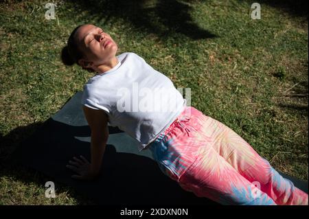 Eine Frau, die eine Yoga-Dehnung auf einer Matte in ihrem Garten macht. Sie saugt das Sonnenlicht auf und genießt ein Workout im Freien. Stockfoto