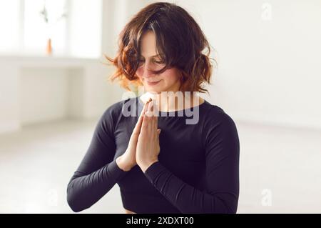 Sportliche Frau sitzt im Fitnessstudio mit geschlossenen Augen, meditiert und übt Yoga in Lotus-Pose drinnen. Stockfoto