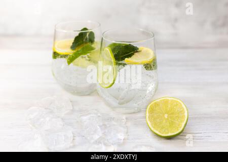 Kaltes erfrischendes Limonadengetränk oder Cocktail aus Mineralwasser, Zitrusfrüchten und Minze. Trinkglas mit Eiswürfeln serviert. Auf weißem Holzhintergrund. Stockfoto
