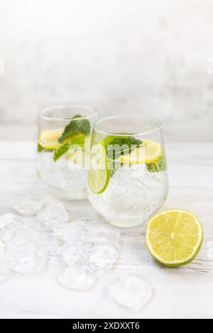 Kaltes erfrischendes Limonadengetränk oder Cocktail aus Mineralwasser, Zitrusfrüchten und Minze. Trinkglas mit Eiswürfeln serviert. Auf weißem Holzhintergrund. Stockfoto