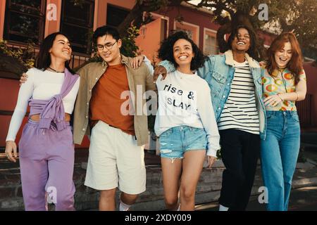 Glückliche Gruppe von Freunden, die Arm in Arm in der Stadt spazieren, lächeln und einen sonnigen Tag genießen. Momente der Freundschaft und Freude festhalten. Stockfoto