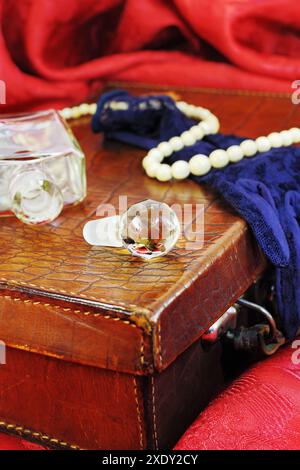 Vintage Flasche Parfüm und weißen Knochen Halskette auf Leder Koffer in künstlerischer Verwirrung auf rot Textil Stockfoto