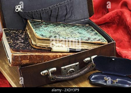 Lederkoffer mit alten Büchern und anderen Vintage-Sachen auf Rot Stockfoto