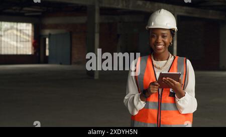 Selbstbewusste Ingenieurin, die Sicherheitsausrüstung mit Tablet auf der Baustelle trägt Stockfoto