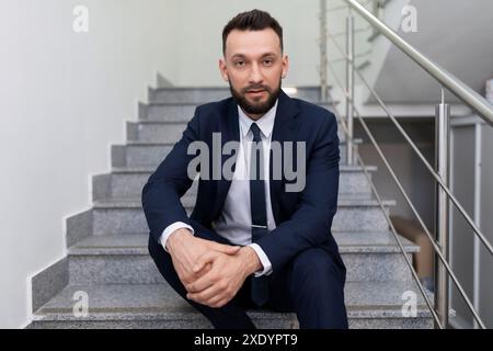 Ein männlicher Geschäftsmann, der auf der Treppe sitzt, tritt in die Kamera ein Stockfoto