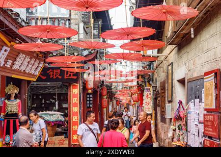 Fenghuang, China - 23. September 2017: Herrlicher Blick auf die gemütliche, enge Straße, die mit traditionellen orientalischen chinesischen roten Regenschirmen dekoriert ist. Stockfoto