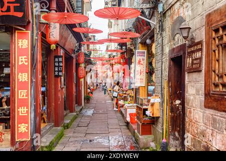 Fenghuang, China - 23. September 2017: Herrlicher Blick auf die gemütliche, enge Straße, die mit traditionellen orientalischen chinesischen roten Regenschirmen dekoriert ist. Stockfoto